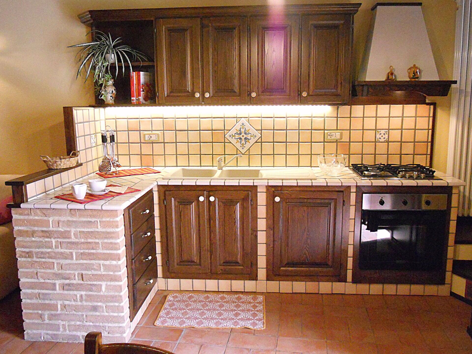 Eine Küche mit Holzausstattung, Fliesenrückwand, Backsteinwand, Gasherd und eingebautem Ofen.