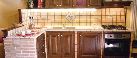 A kitchen with wooden cabinets, a tiled backsplash, a brick accent wall, a gas stove, and a built-in oven.