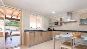 A modern kitchen with wooden cabinets, a stainless steel range hood, and a dining area with a table and chairs. - VILLA GLORIA - Villa with private pool in Cala Pi - Llucmajor. Free WiFi (Cala Pi)