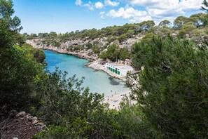 A coastal area with a beach, a small building with green doors, and surrounding greenery. - VILLA GLORIA - Villa with private pool in Cala Pi - Llucmajor. Free WiFi (Cala Pi)