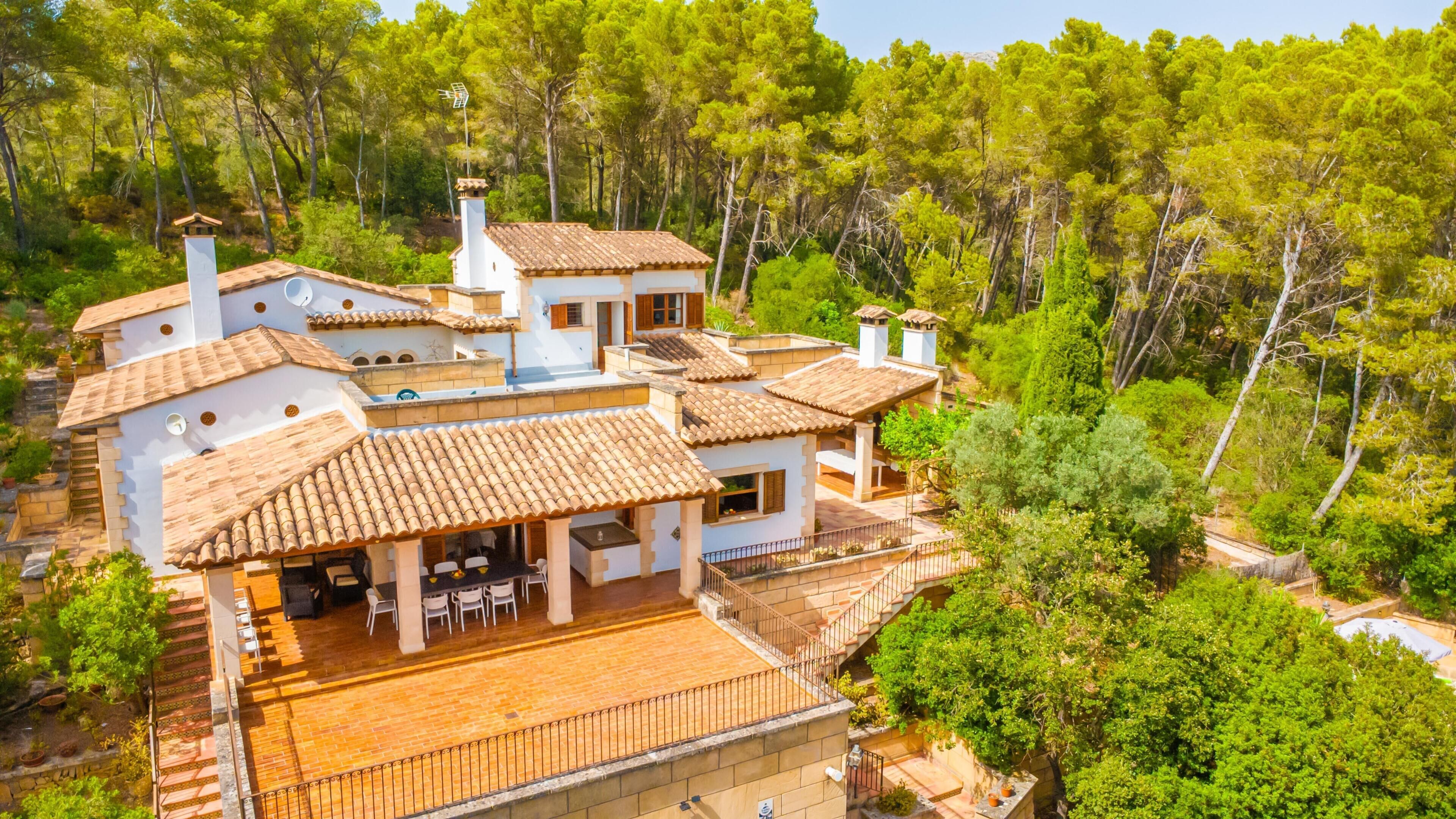 Una casa de varios pisos con una terraza, rodeada de abundante vegetación.