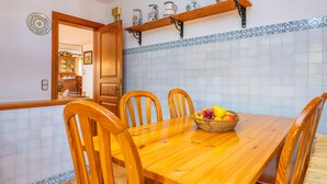 A dining area with a wooden table and chairs, a fruit basket, and a kitchen visible in the background. - CAN PERE VELL - Villa with private pool in ANDRATX. Free WiFi (Andratx)