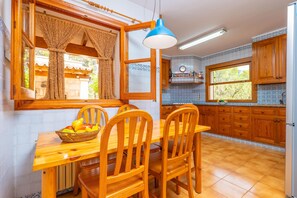 A kitchen with wooden cabinets, a dining table with chairs, a fruit basket, and a blue pendant light. - CAN PERE VELL - Villa with private pool in ANDRATX. Free WiFi (Andratx)