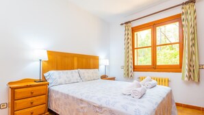A bedroom with a wooden headboard, a single bed with floral bedding, a nightstand with a lamp, a window with curtains, and a radiator. - CAN PERE VELL - Villa with private pool in ANDRATX. Free WiFi (Andratx)
