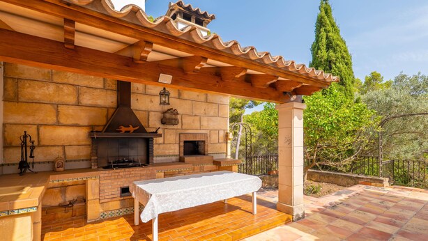 An outdoor kitchen with a brick fireplace, a table, and a pergola structure. - CAN PERE VELL - Villa with private pool in ANDRATX. Free WiFi (Andratx)