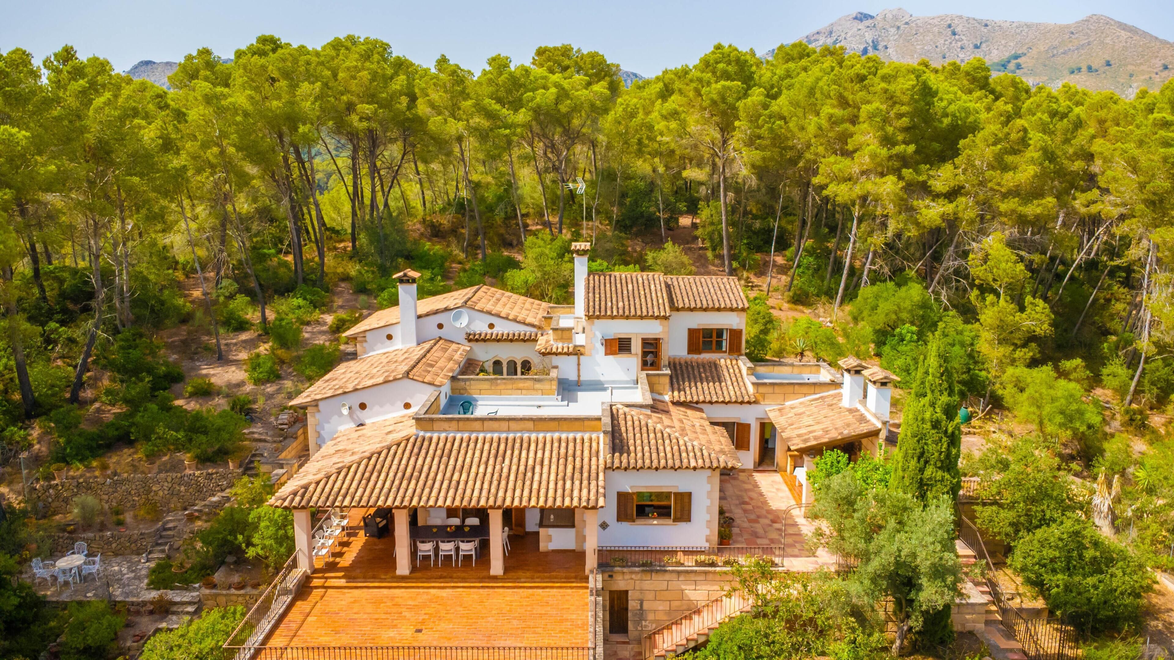 A multi-story house with a patio area, surrounded by trees and a mountainous backdrop.