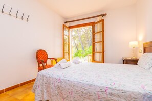 A hotel room with a bed, a chair, a nightstand, a lamp, and a window with a view of trees.