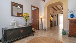 Une pièce comprenant une commode en bois, un miroir, un vase avec des tournesols, une lampe et un vase vert posé sur la commode.