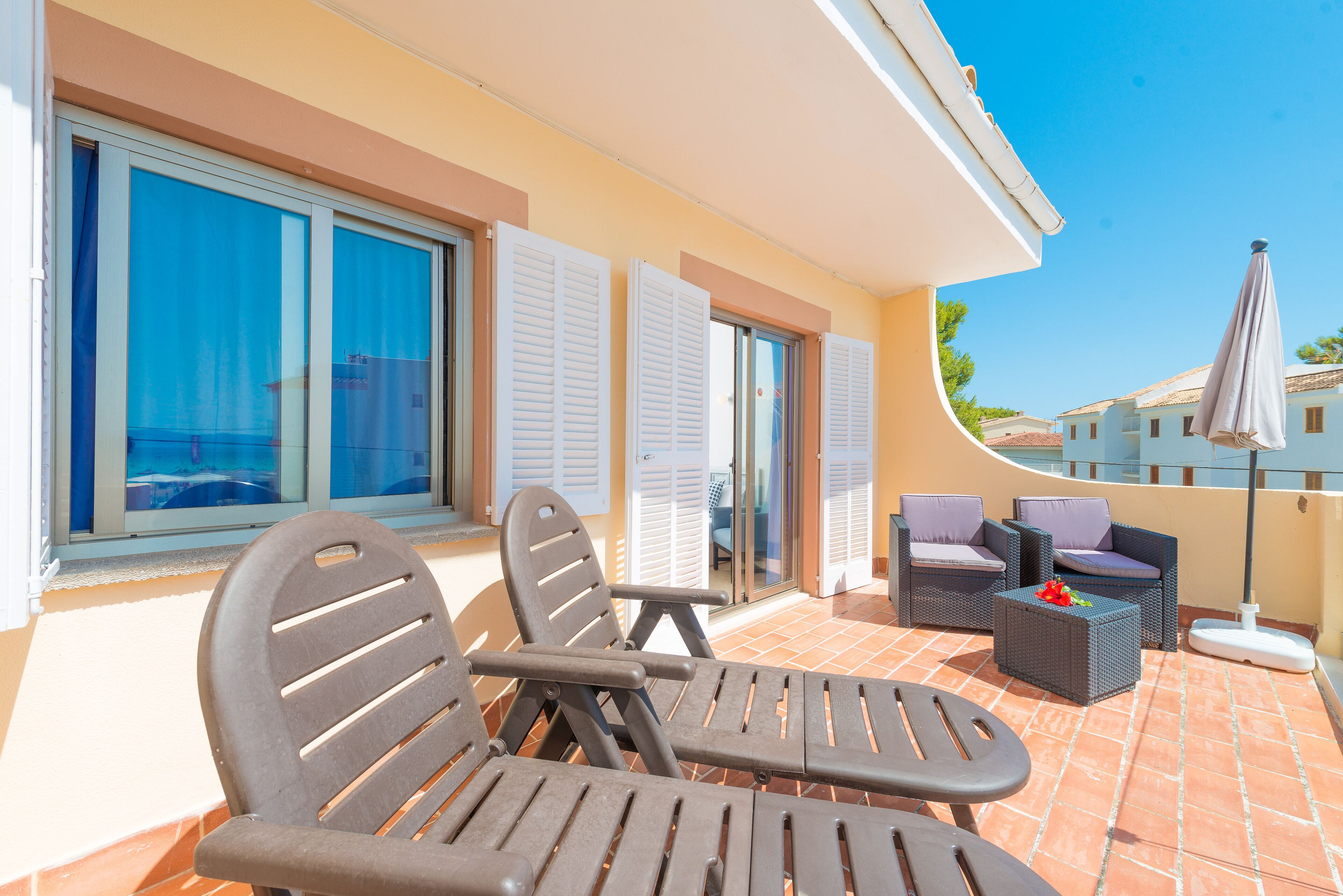 A terrace with outdoor furniture, a view of the sea, and a building with a tiled roof.