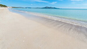 Ein Strand mit klarem Wasser, sandigem Ufer und Bergen im Hintergrund.