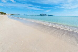 A beach with clear water, a sandy shore, and distant mountains.