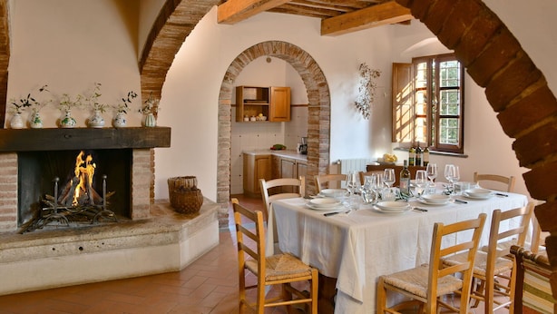 A dining area with a brick fireplace, wooden beams, and a table set for four. - Stunning private villa for 12 guests with private pool, WIFI, TV, terrace and panoramic view (Montelopio)