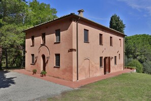 Traditional two-story building with a flat roof and symmetrical facade, set amidst a serene and lawn with mature trees.