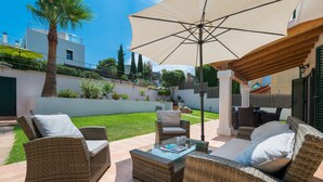 An outdoor patio with wicker furniture, a large umbrella, and a view of a modern building in the background. - EL PINAR  - Villa with private pool in Cala Sant Vicenç. Free WiFi (Pollen��a)