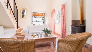 A cozy living room with a white sofa, wicker chairs, a coffee table with drinks, a fireplace, and a staircase. - EL PINAR  - Villa with private pool in Cala Sant Vicenç. Free WiFi (Pollen��a)