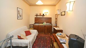 A cozy living room with a sofa, a small table, a rug, and a kitchen area with a wooden cabinet and a sink. - Lovely apartment for 3 people with hot tub, WIFI, A/C and TV (Cortona)