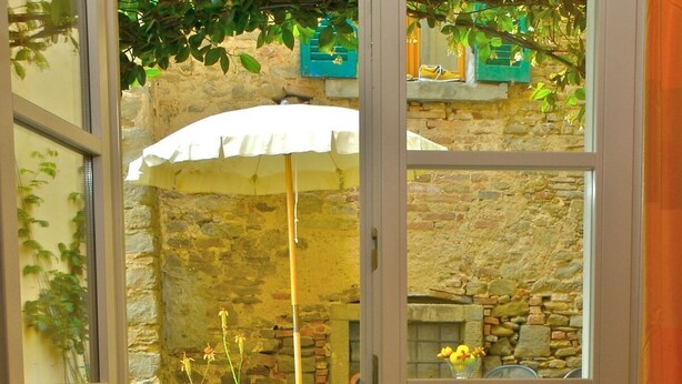 A view from a room with a metal balcony railing, a stone wall, and a table with chairs and a basket of fruit. - Lovely apartment for 3 people with hot tub, WIFI, A/C and TV (Cortona)