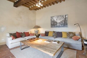 A cozy living room with a wooden coffee table, two sofas with patterned cushions, a lamp, and a framed picture on the wall.