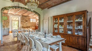 A dining area with a long table set for a meal, a wooden cabinet with glass doors, and a stone wall in the background.