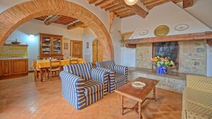 A cozy living room with a fireplace, striped sofas, and a dining area with wooden cabinets. - Nice apartment for 7 guests with WIFI, pool, close to Siena (Monteroni D'arbia)