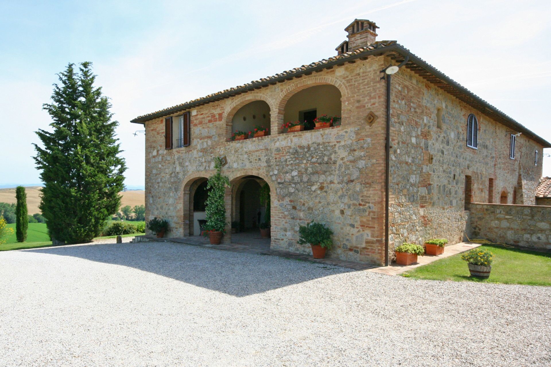 A stone building with a tiled roof, two arches, and potted plants.