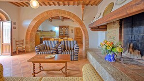 A cozy living room with a fireplace, a striped sofa, a wooden table, and a tiled floor. - Nice apartment for 7 guests with WIFI, pool, close to Siena (Monteroni D'arbia)