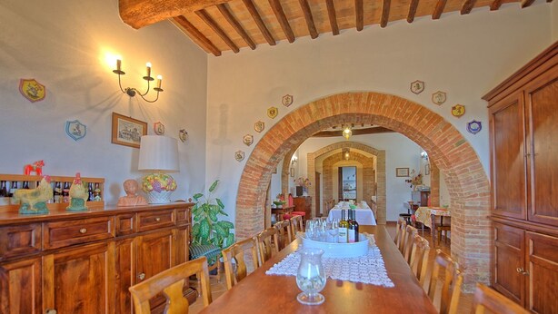Comedor con una larga mesa de madera dispuesta para una comida, flanqueada por armarios de madera y un arco de ladrillo.