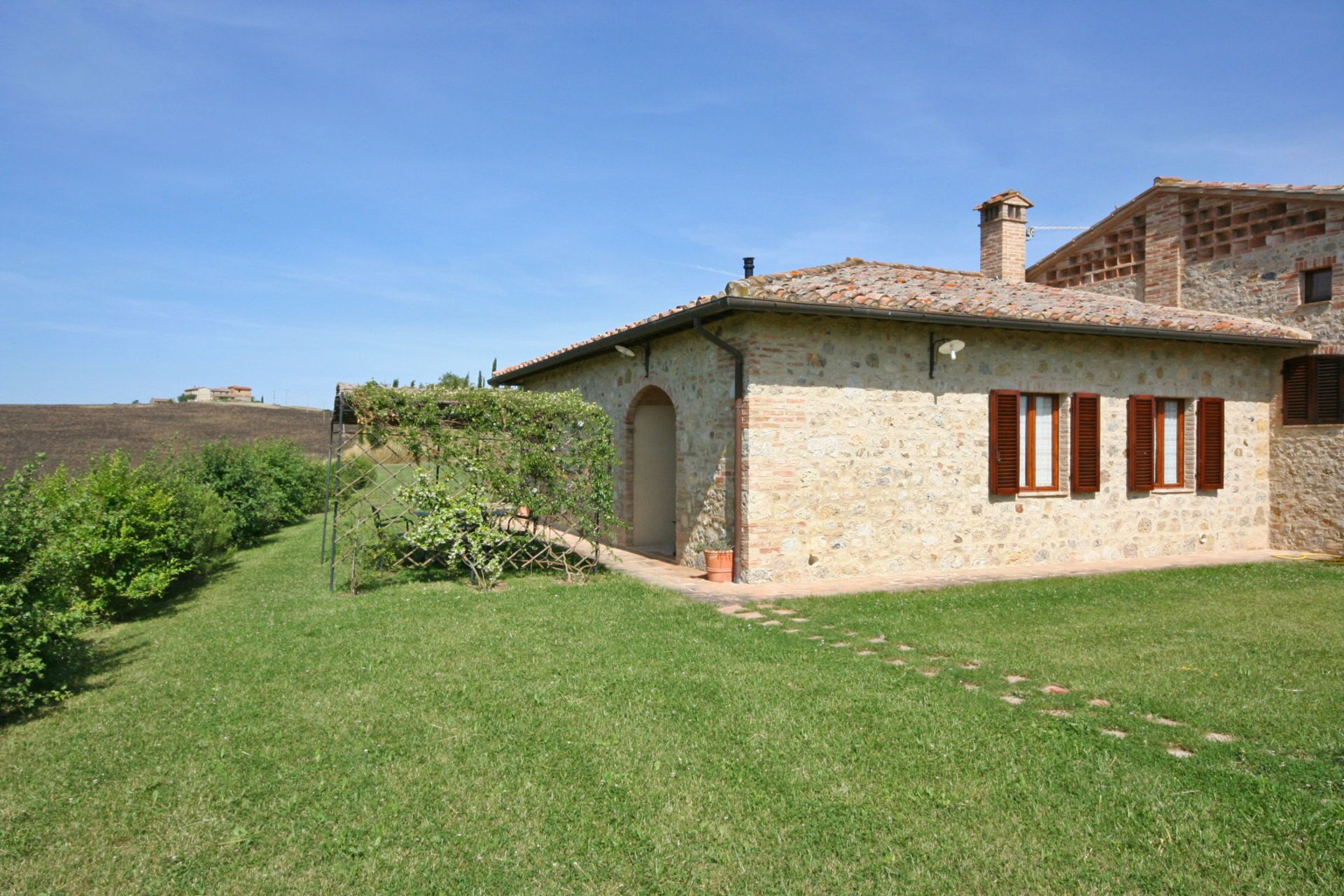 A stone house with a tiled roof, a small garden, and a clear sky.