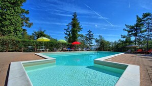 En rektangulär swimmingpool med ett klart, blått vatten, omgiven av en terrass av tegelsten. Runt poolområdet finns solstolar och parasoller.