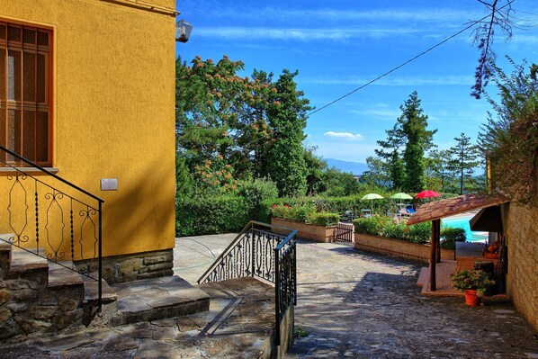 A courtyard with a yellow building, stone steps, and a covered seating area with umbrellas.