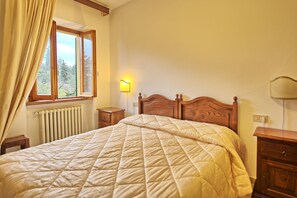 Une chambre à coucher avec un lit en bois, une table de chevet, une commode, une fenêtre avec des rideaux et une lampe fixée au mur.