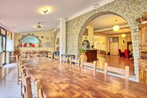 A spacious dining area with a long wooden table, stone arches, and a view of the adjacent room.