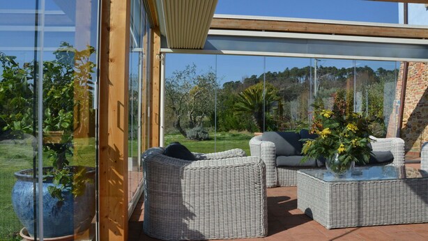A modern outdoor seating area with wicker furniture and a glass table, overlooking a lush garden and distant hills. - Stunning private villa with A/C, WIFI, private pool, TV, patio, pets allowed and panoramic view (Altopascio)