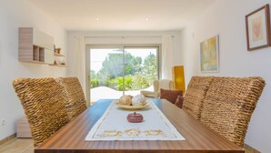 A modern dining area with a wooden table, woven chairs, and a view of greenery through the window. - CASA GARONDA - Beautiful chalet with private pool near the beach Free WiFi (Cala Pi)