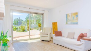 A modern living room with a white sofa, a beige armchair, and a large window offering a view of greenery. - CASA GARONDA - Beautiful chalet with private pool near the beach Free WiFi (Cala Pi)