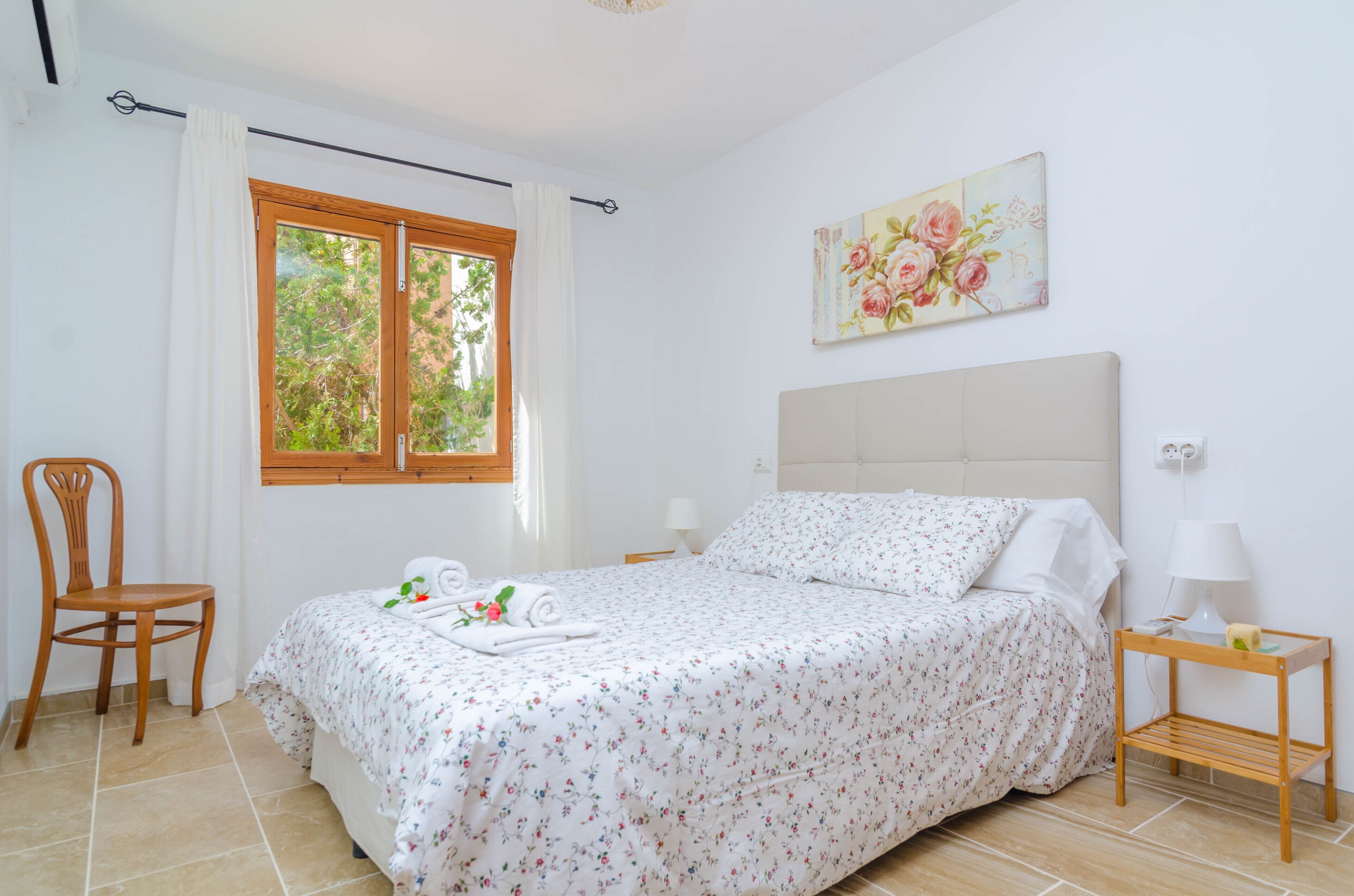 Een slaapkamer met een bed, een stoel, een raam, een schilderij en een nachtkastje.