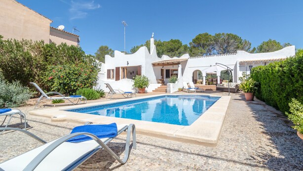 A pool area with lounge chairs, a small patio with outdoor furniture, and a building with white walls and a tiled roof. - CASA GARONDA - Beautiful chalet with private pool near the beach Free WiFi (Cala Pi)