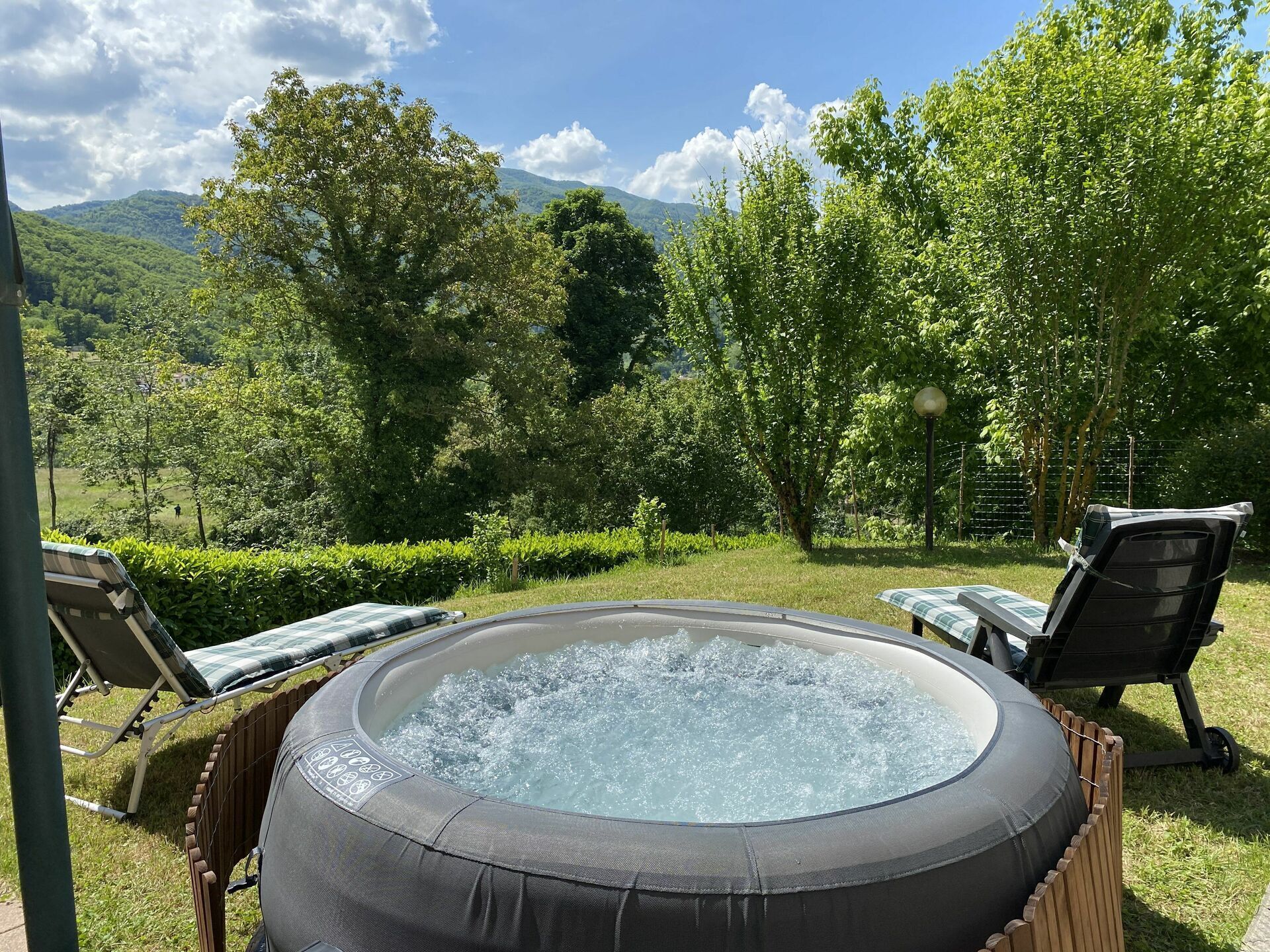 A hot tub surrounded by lounge chairs, set against a backdrop of lush greenery and distant mountains.