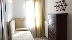 Un dormitorio con cama, cómoda, radiador y ventana con cortinas.