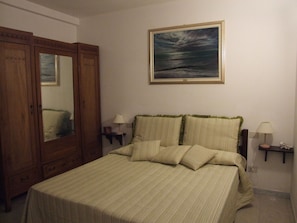 Une chambre à coucher avec un lit, une armoire, une table de chevet, une lampe et un tableau au mur.