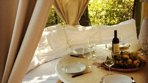 Una mesa redonda dispuesta para una comida, con platos, cubiertos, vino y una cesta de frutas.