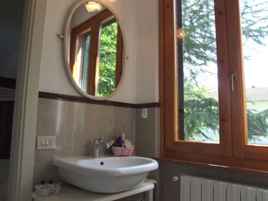 A bathroom with a white sink, a mirror above it, and a window with wooden frames. - Lovely apartment for 5 people with pool, WIFI, TV and patio (Sassetta)