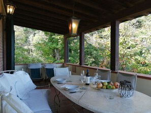 An outdoor dining area with a table set for two, surrounded by chairs, a hanging light fixture, and a view of trees. - Beautiful apartment for 5 guests with pool, WIFI, TV and patio (Sassetta)