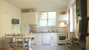 A compact kitchen with white cabinets, a dining table with chairs, a washing machine, an oven, and a wood-burning stove. - Nice apartment for 6 guests with WIFI and TV (Sassetta)