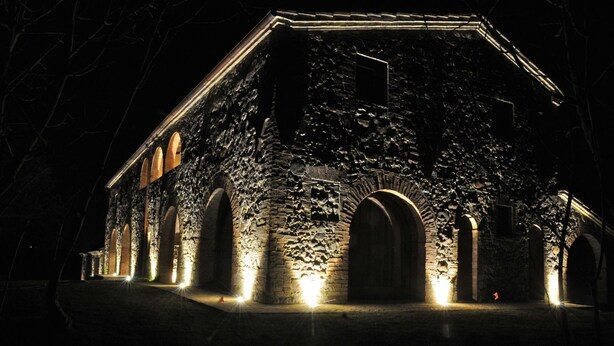 Edificio de piedra con varios arcos y un gran arco central, iluminado por luces exteriores.