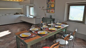 Comedor con una mesa preparada para seis personas, cocina al fondo y un ventanal con vistas.