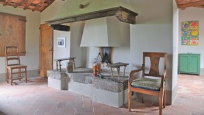 Un interior rústico con chimenea de piedra, sillas de madera y un armario verde.
