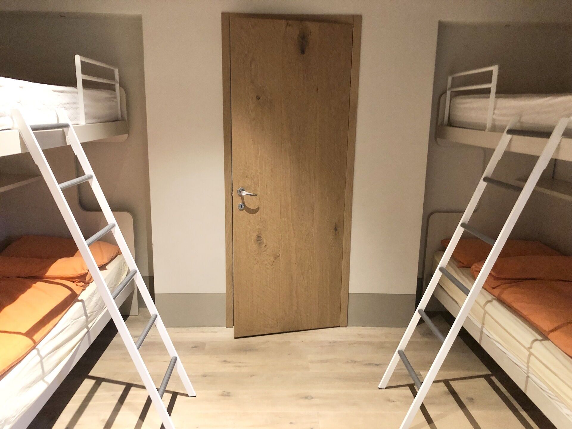Ein Zimmer mit zwei Etagenbetten, einer Holztür und einem hellen Boden.