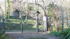 Una entrada protegida con una cerca de metal, un muro de piedra y un camino que lleva a un edificio.