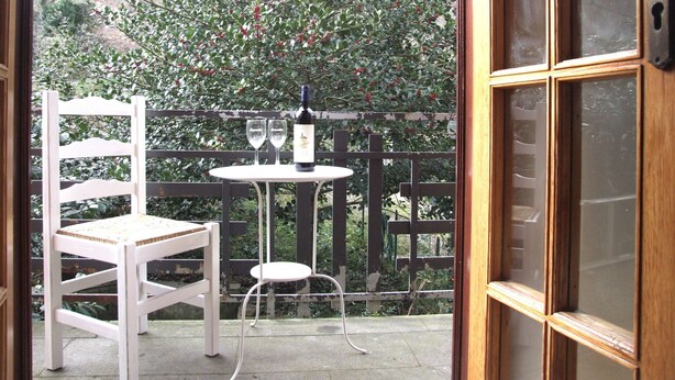 Un patio con una silla blanca, una mesita y una botella de vino.